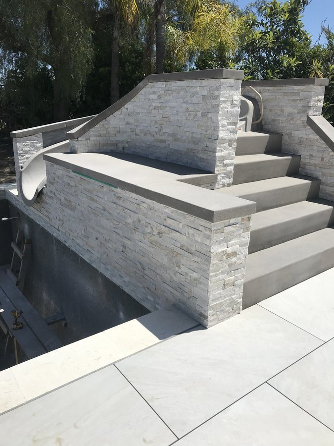 Stacked-stone veneer spa wall with concrete steps and coping