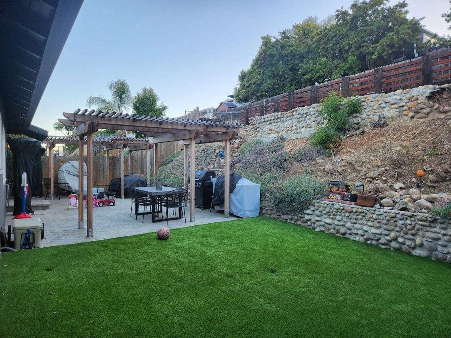 Backyard pergola over a paver patio with turf lawn and stone walls