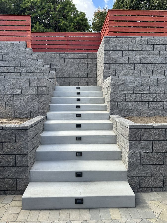 Terraced CMU block retaining walls with a concrete stairway on a hillside lot